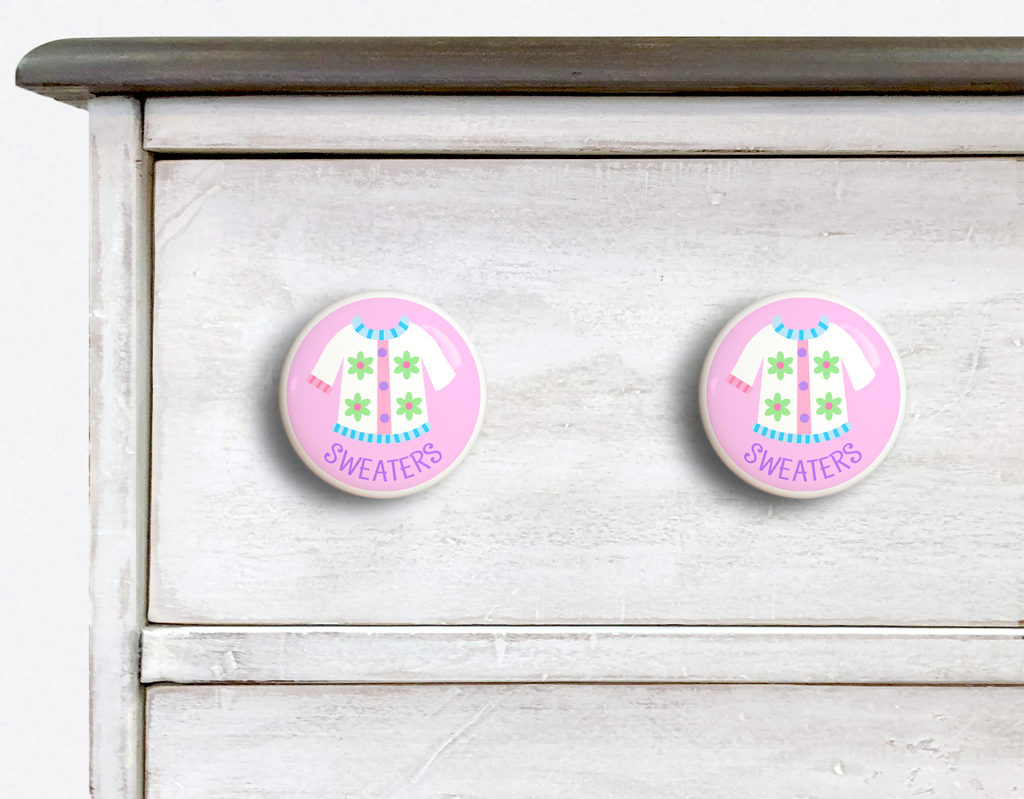 2 Ceramic drawer knobs on a dresser, girls sweater on a pink ground with the word Sweaters written below