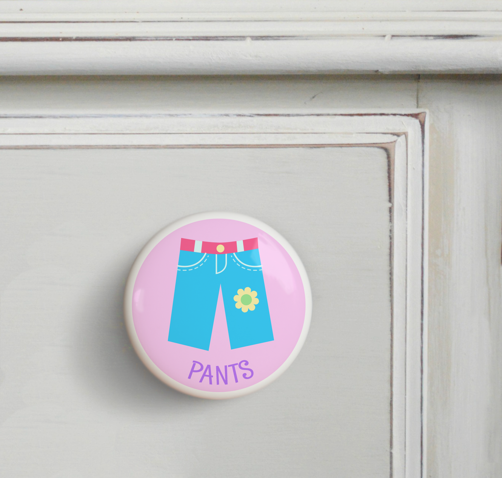 2 Ceramic drawer knobs on a dresser, girl's pants on a pink ground with the word Pants written below