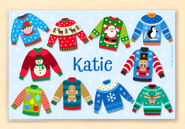 Personalized place mat with 10 ugly christmas sweaters on a light blue background with white snowflakes. Name is in the center in dark blue. 