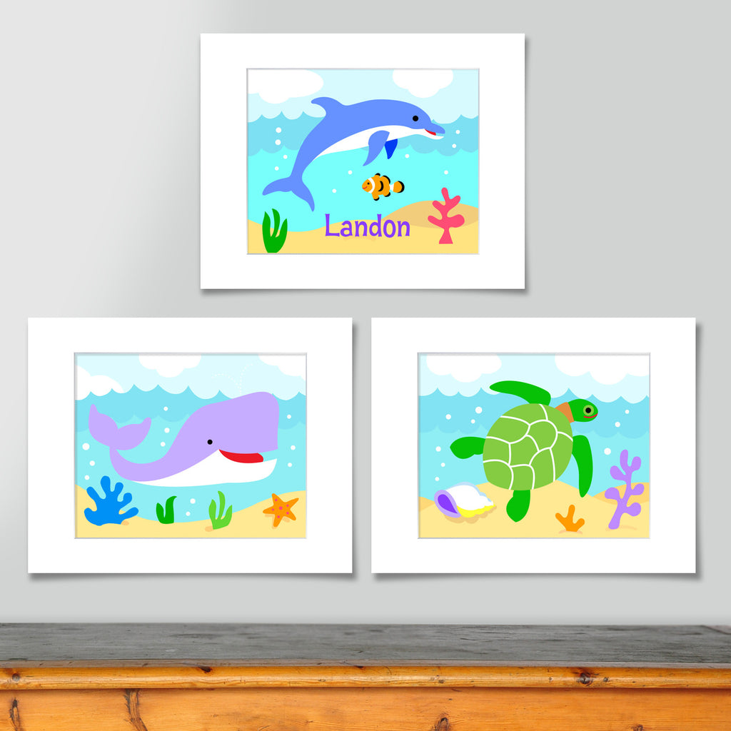 Set of 3 ocean themed prints. Blue dolphin personalized with your childs name, purple whale, and green sea turtle. Each on a sea blue scenic background.