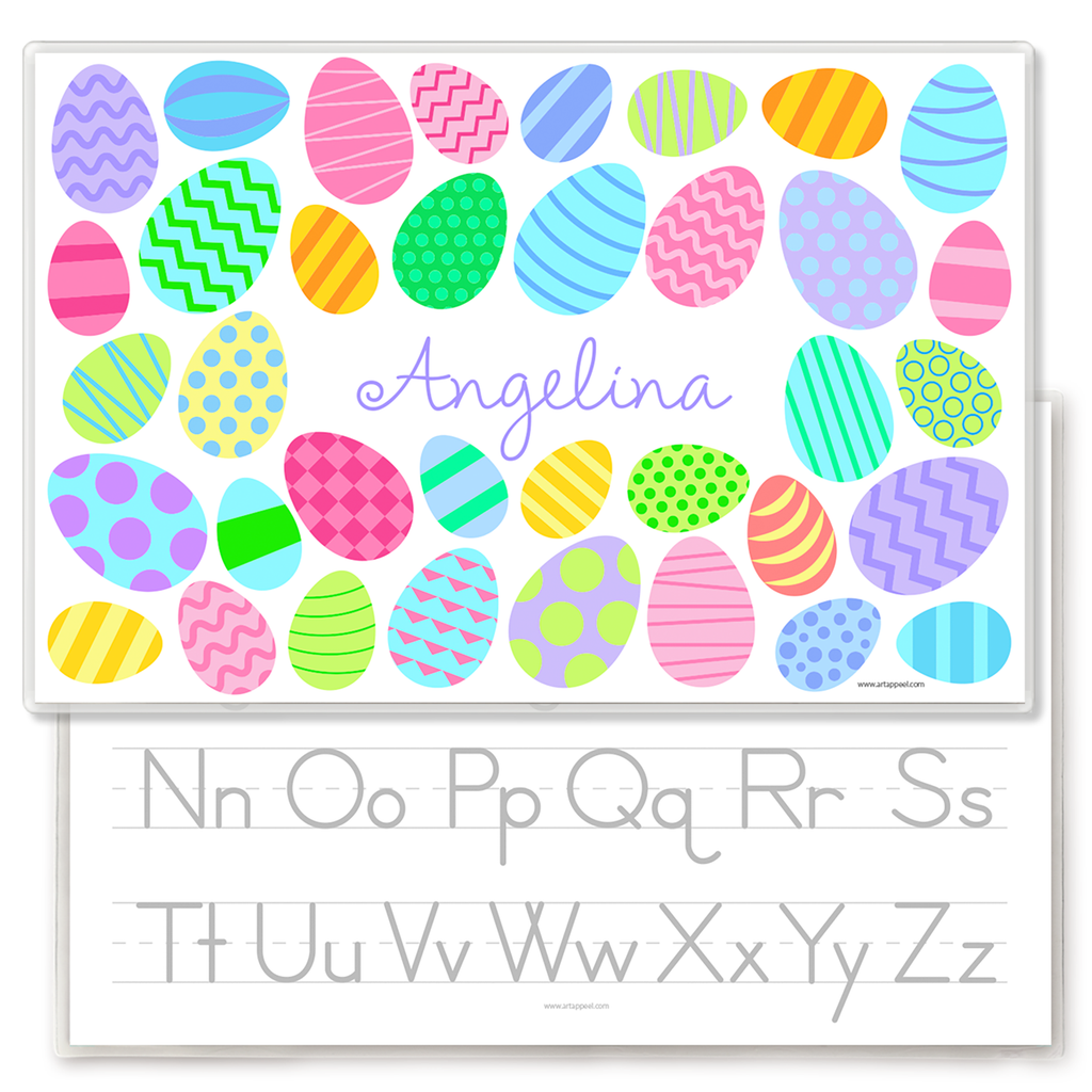 Personalized Easter placemat featuring colorful patterned eggs in pastel shades of pink, blue, green, yellow, and purple surrounding the name Angelina in a playful script font. The festive Easter egg designs include stripes, polka dots, zigzags, waves, and geometric patterns on a light gray background. Laminated kids placemat shown over an alphabet handwriting practice sheet.