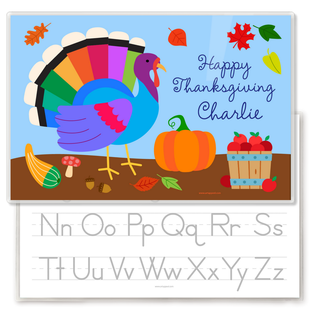 Colorful Thanksgiving-themed children's placemat with a rainbow turkey, pumpkins, falling leaves, and a bucket of apples, plus a preview of the back side of the placemat that features a traceable alphabet.