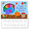 Colorful Thanksgiving-themed children's placemat with a rainbow turkey, pumpkins, falling leaves, and a bucket of apples, plus a preview of the back side of the placemat that features a traceable alphabet.