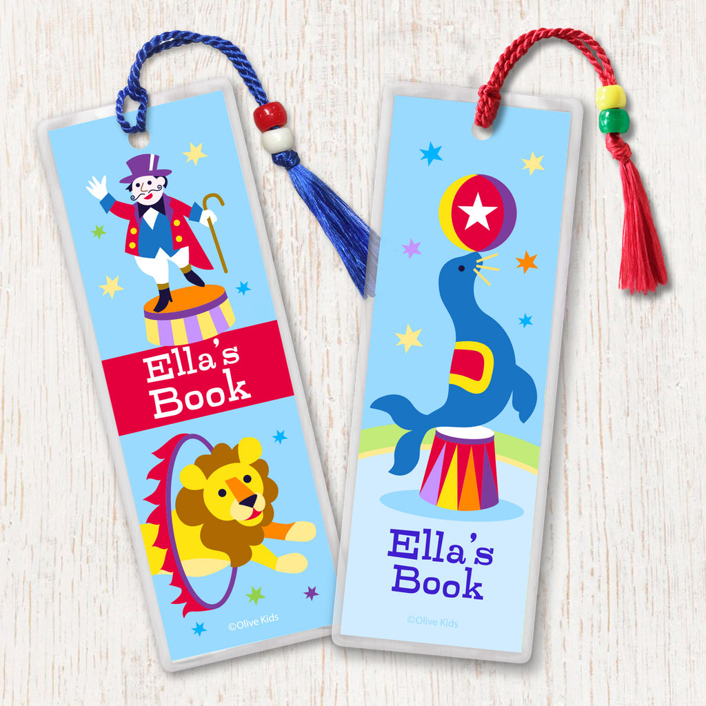 Circus theme kids personalized name bookmarks, one with seal balancing ball and one with ringmaster, both on light blue background.