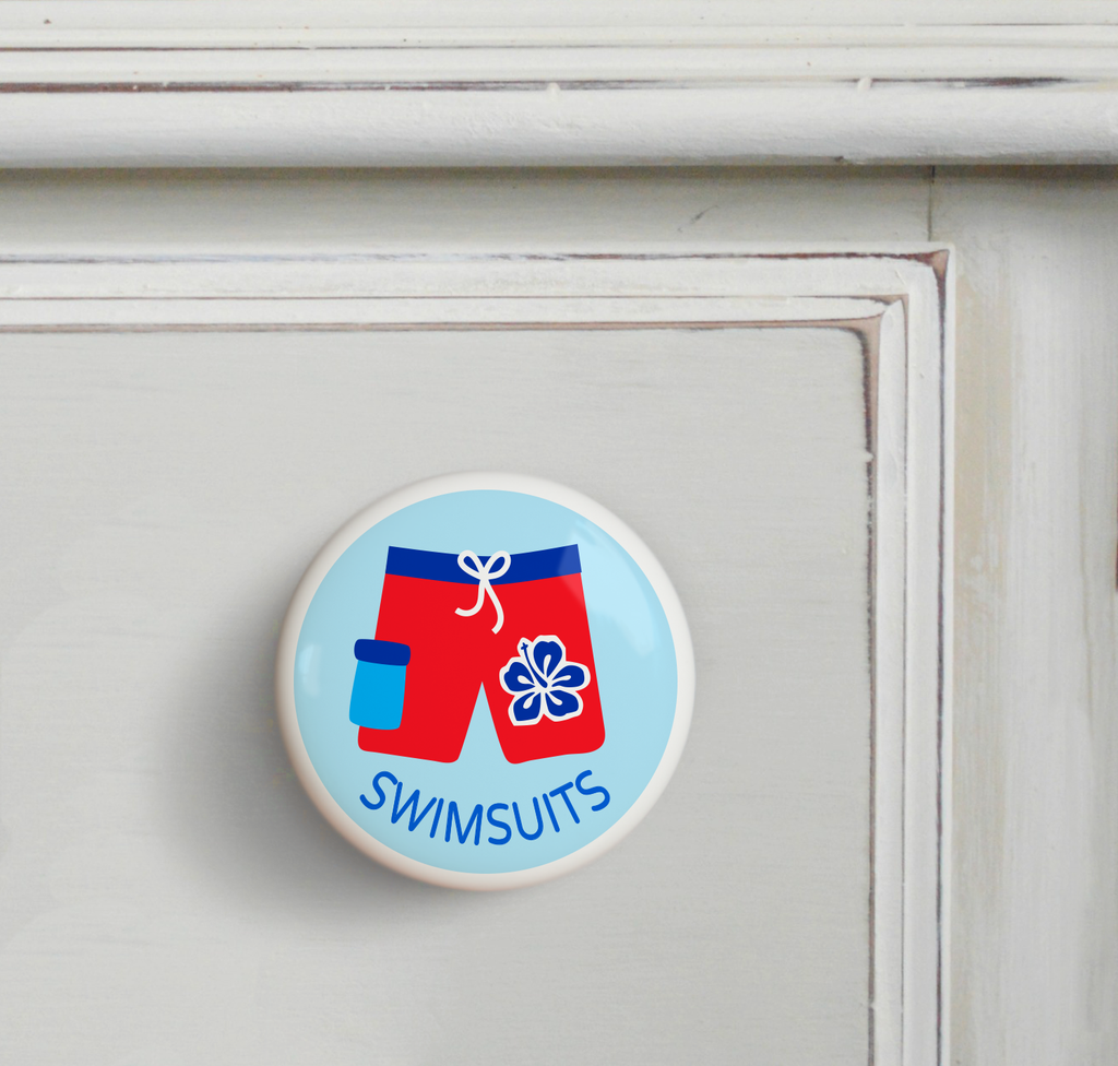 Ceramic drawer knob on a dresser, with boys red bathing suit on a light blue background with the word swimsuits written below