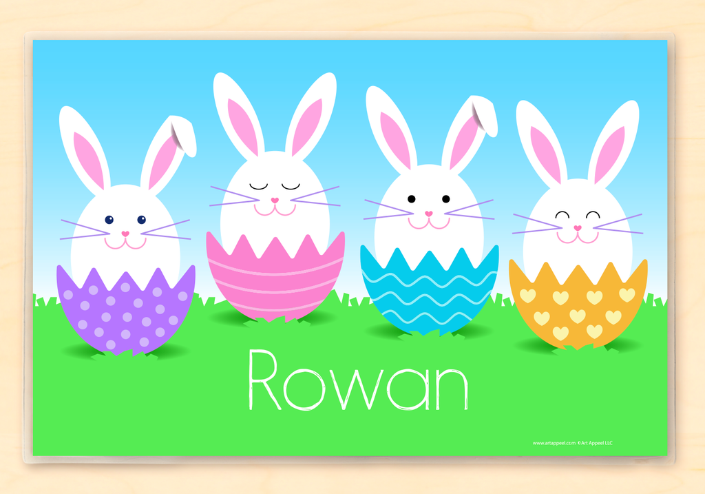 Easter placemat with 4 white bunnies sitting in colorful decorated Easter eggs. Blue sky and green grass background.  Child's name in white letters on green grass.