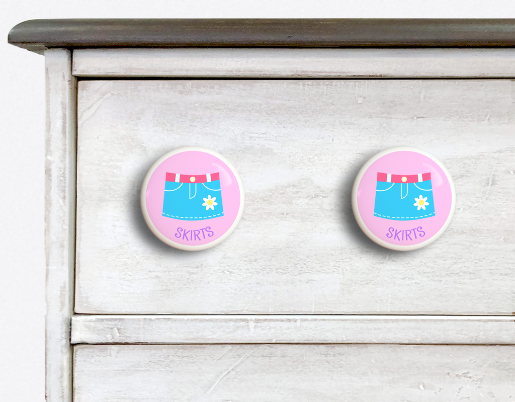 2 Ceramic drawer knobs on a dresser, Girls skirt on a pink ground with the word Skirts written below
