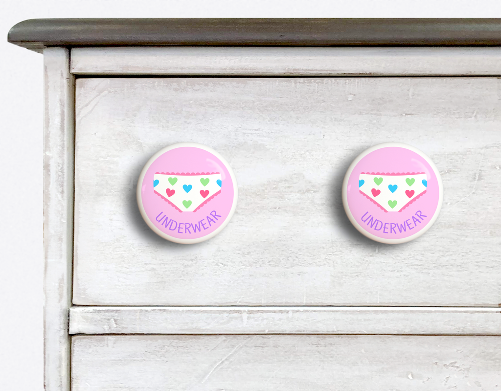 2 Ceramic drawer knobs on a dresser, girls underwear on a pink ground with the word Underwear written below