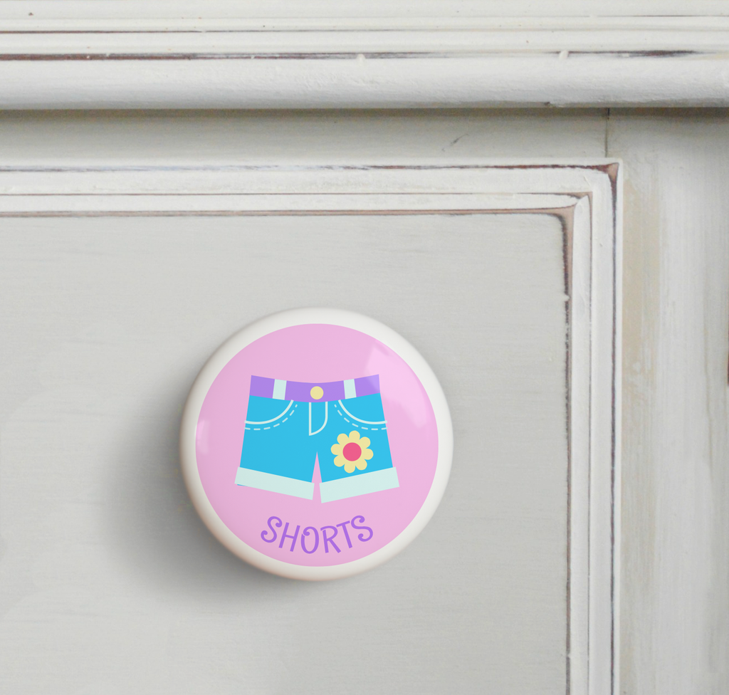 Ceramic drawer knob on a dresser with girl's shorts on a pink background with the word Shorts written below