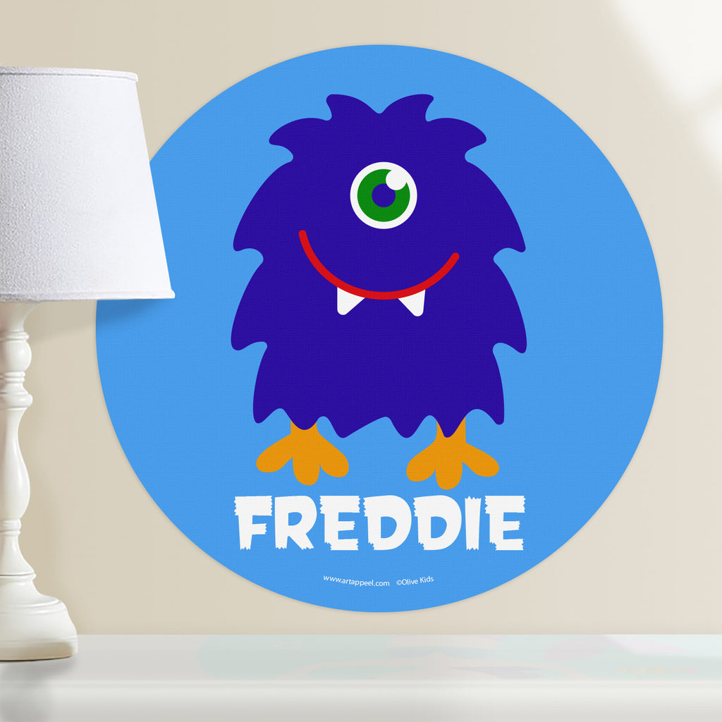 Kids monster personalized wall decal with a happy, shaggy dark blue, one eyed monster on a light blue background.  Circle shape decal.