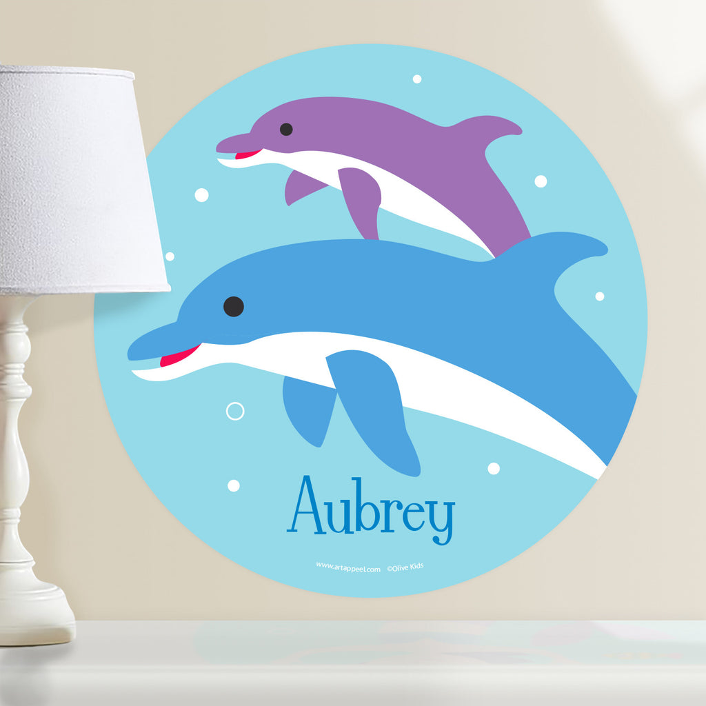 Dolphin personalized kids wall decal features one blue dolphin and one purple dolphin on an ocean blue background.  Circle shape.